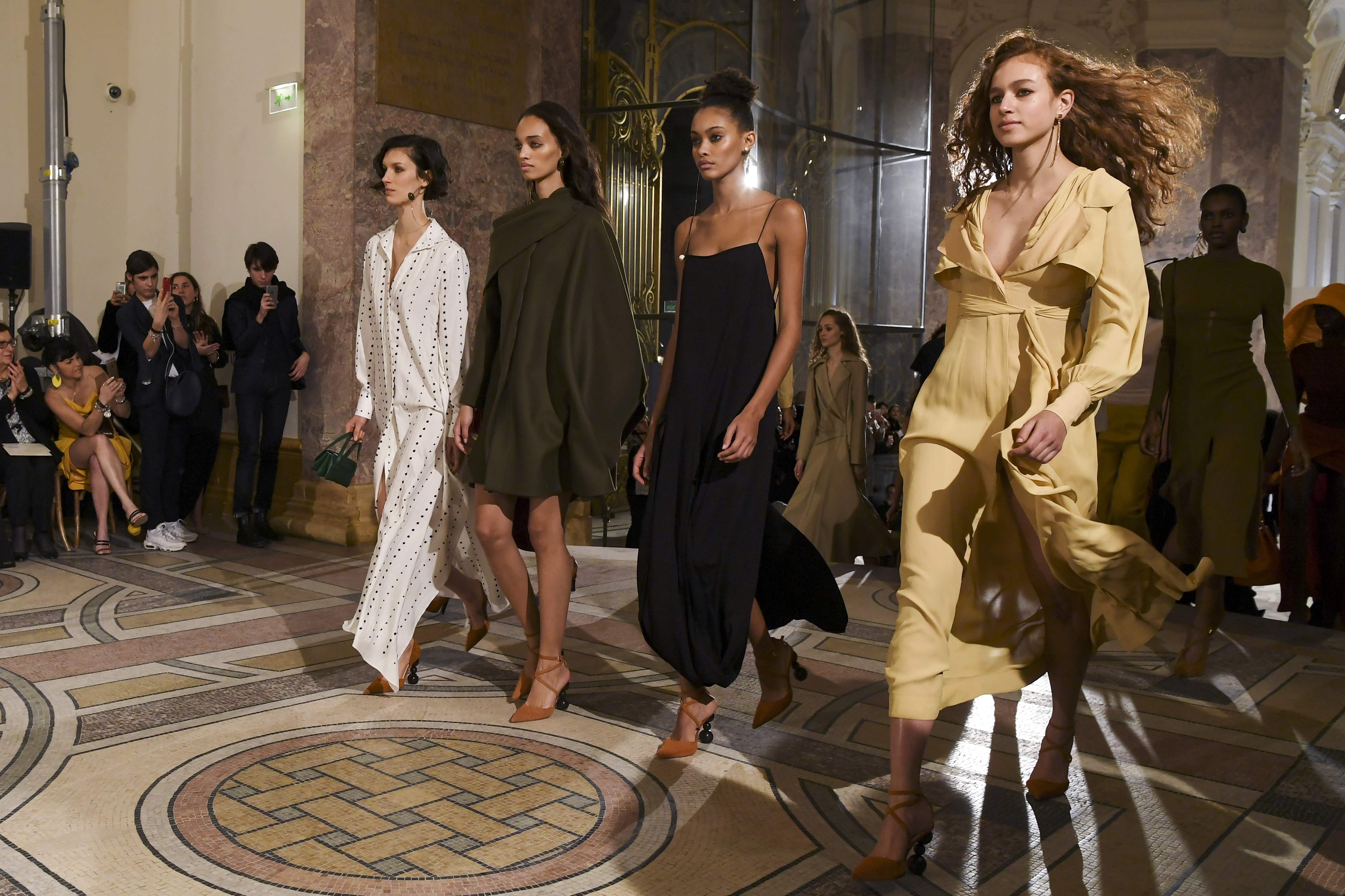 Common elements seen on the catwalk include feminist ideas, scarfs trailing from the forehead, exaggerated hip shapes, and yellow and gold tones