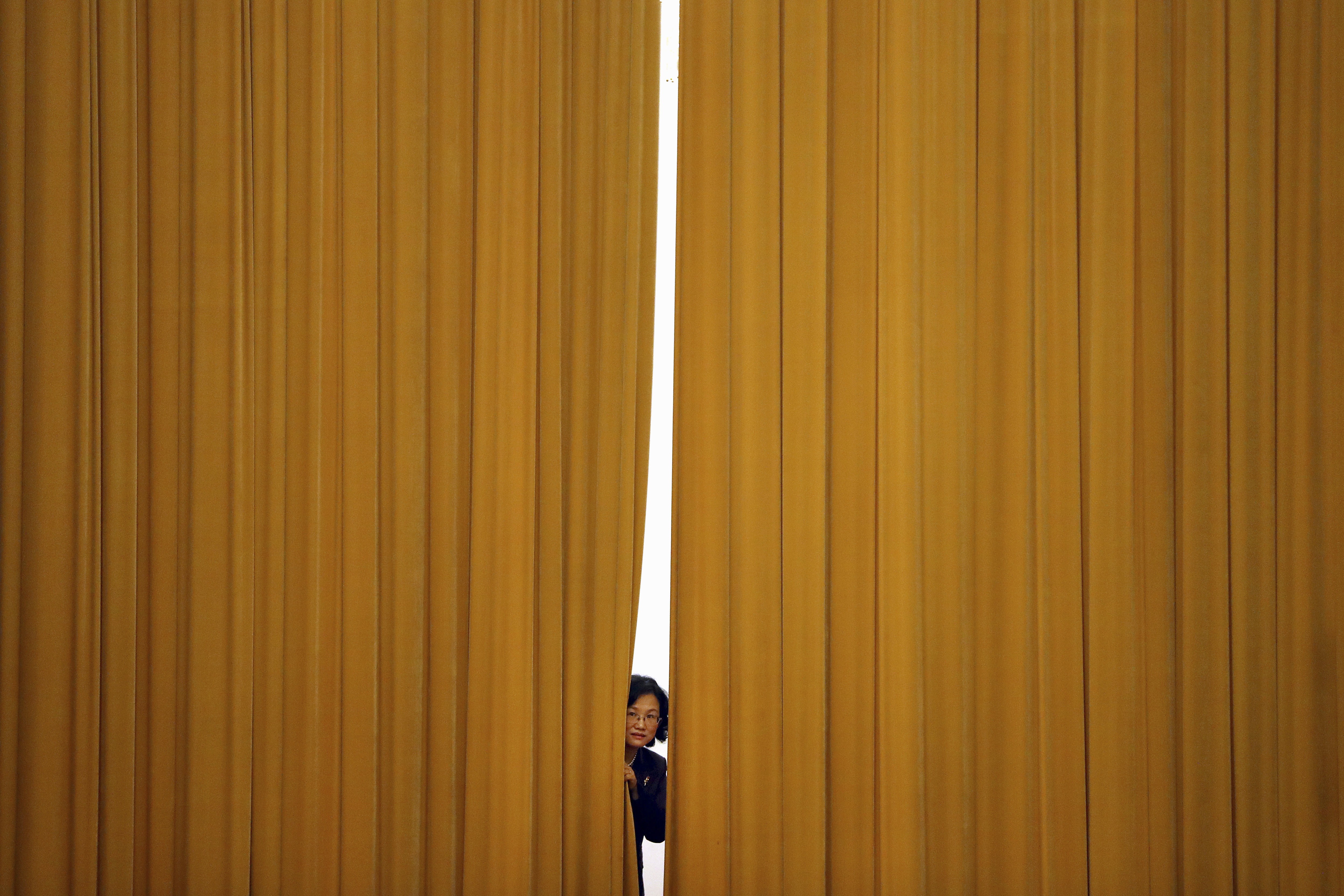 A woman peeps out from behind a curtain ahead of a press conference following a plenary session of China’s National People’s Congress, at the Great Hall of the People in Beijing on March 19. Most people in Western economies know very little of the purposes behind Chinese politics or the meetings of the legislature. Photo: AP