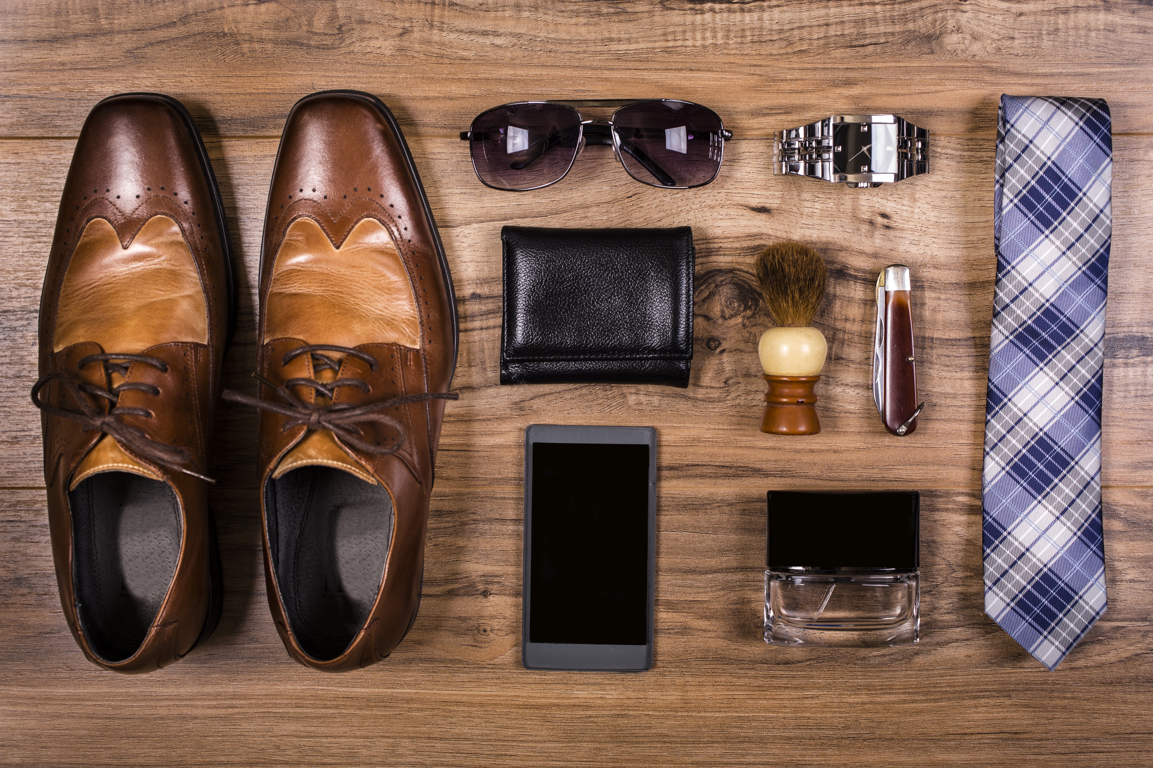 Some stylish Father’s Day gift ideas for your dad (from top left): a pair of brown dress shoes, sunglasses, wallet, smartphone, watch, shaving brush, pocket knife, cologne and a blue plaid tie.