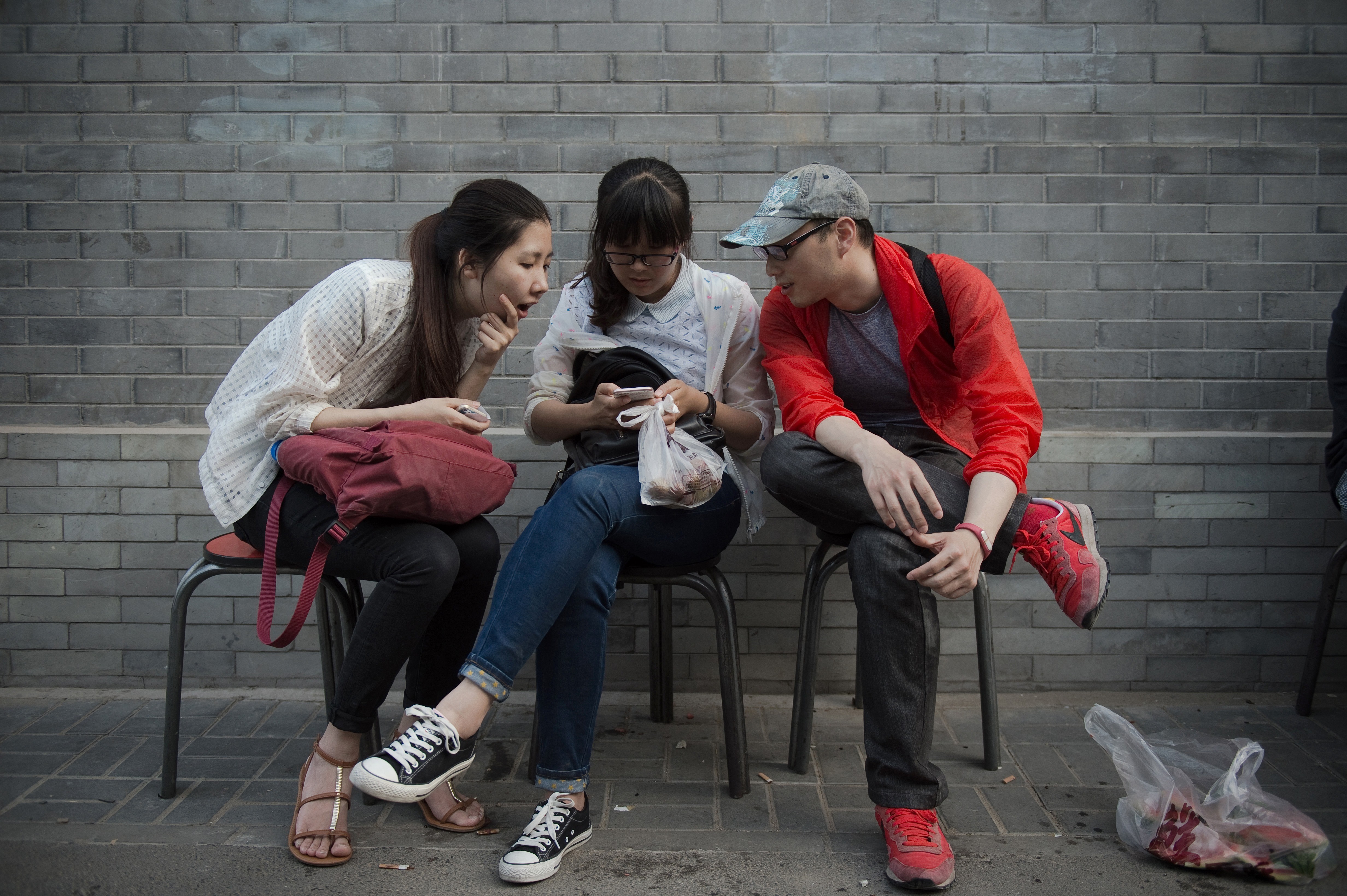 A Chinese woman uses her smartphone as she sits with two friends on a street in Beijing. Photo: AFP