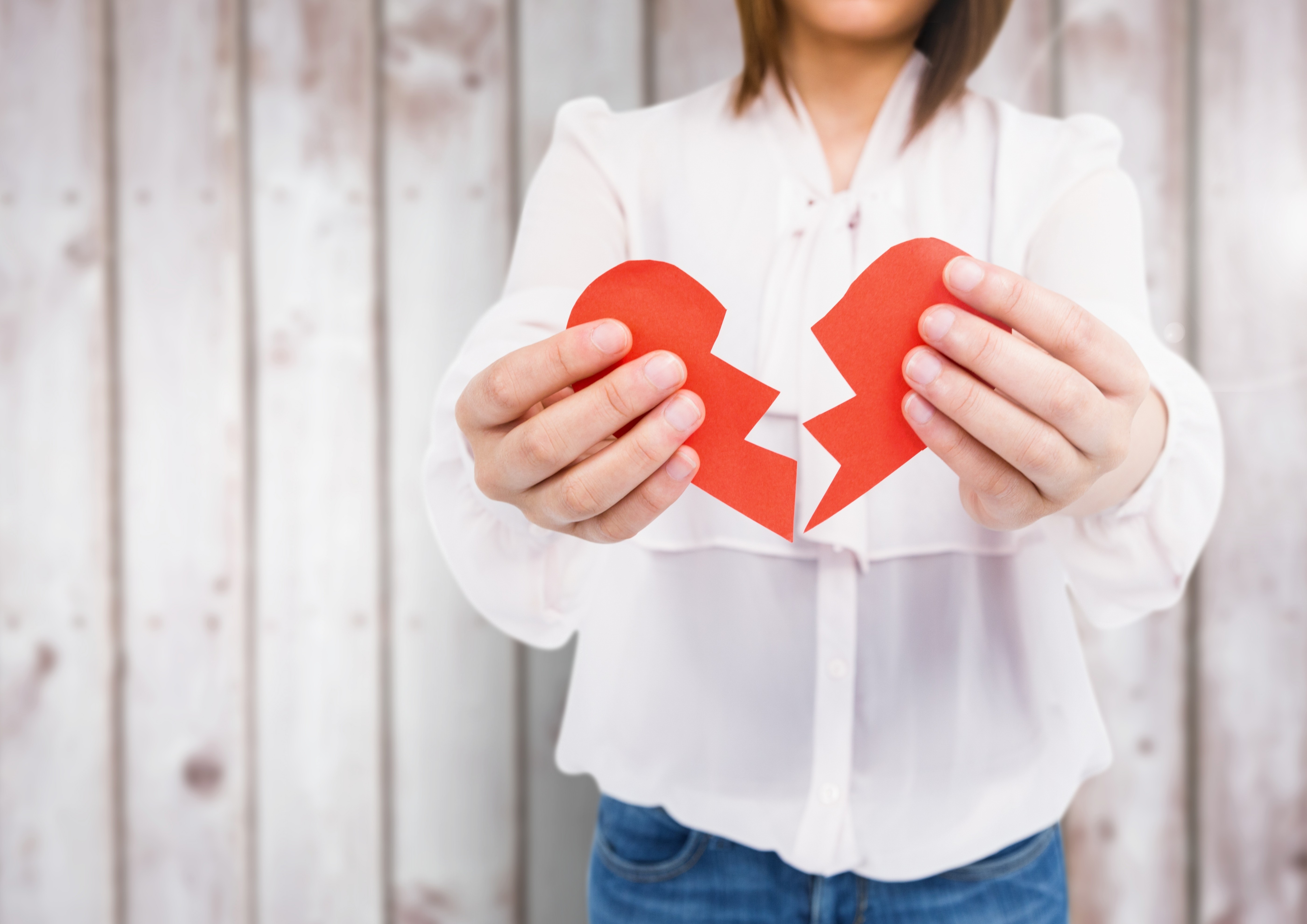 Mid-section of woman holding a broken heart against wooden background. Photo: Shutterstock