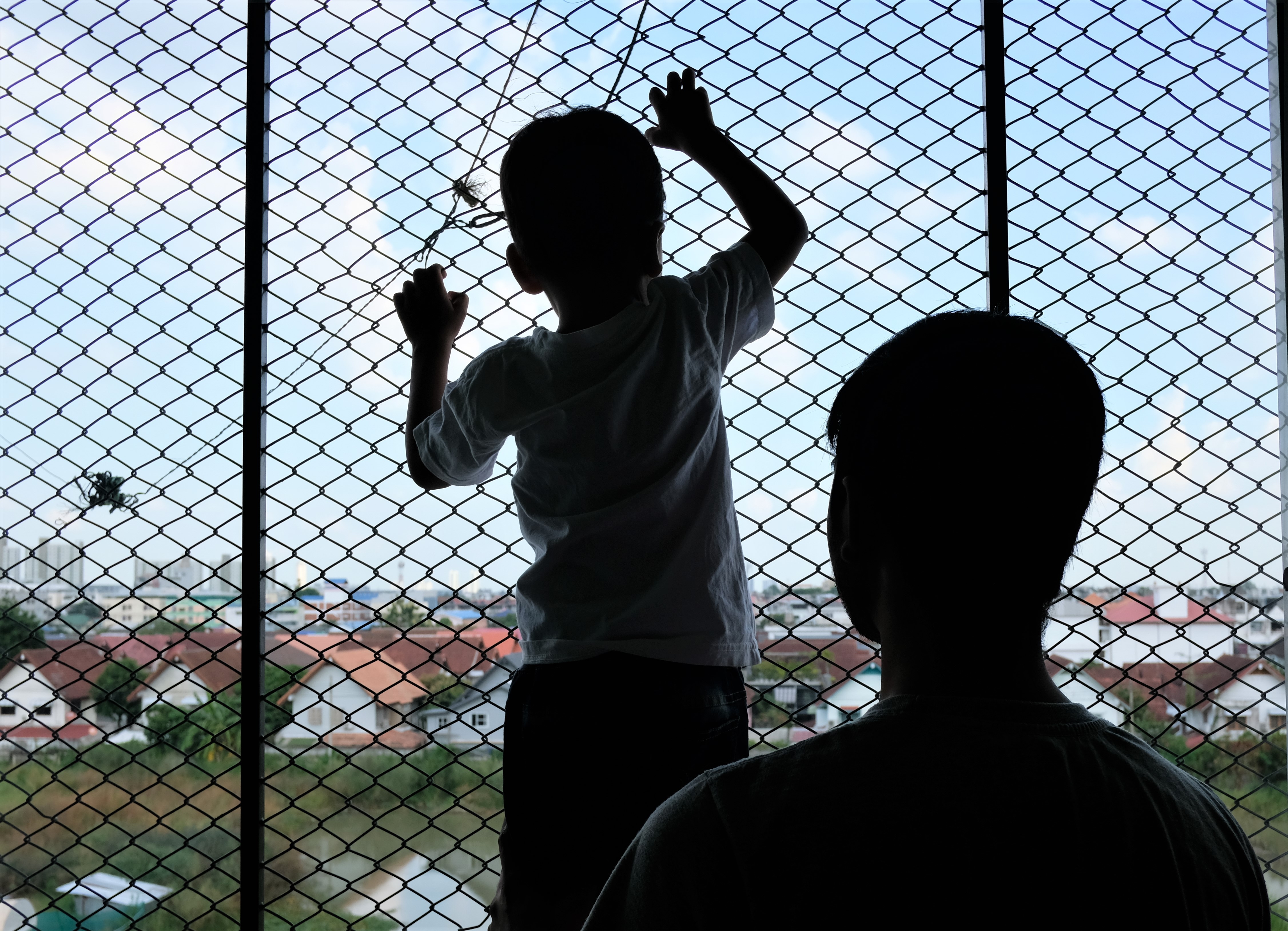 Shazee, a four-year-old stateless boy, gazes through wire-mesh netting in the corridor of a low-rent apartment building in Bangkok, alongside his father, Shan, a Christian asylum seeker from Lahore, Pakistan. Photo: Tibor Krausz