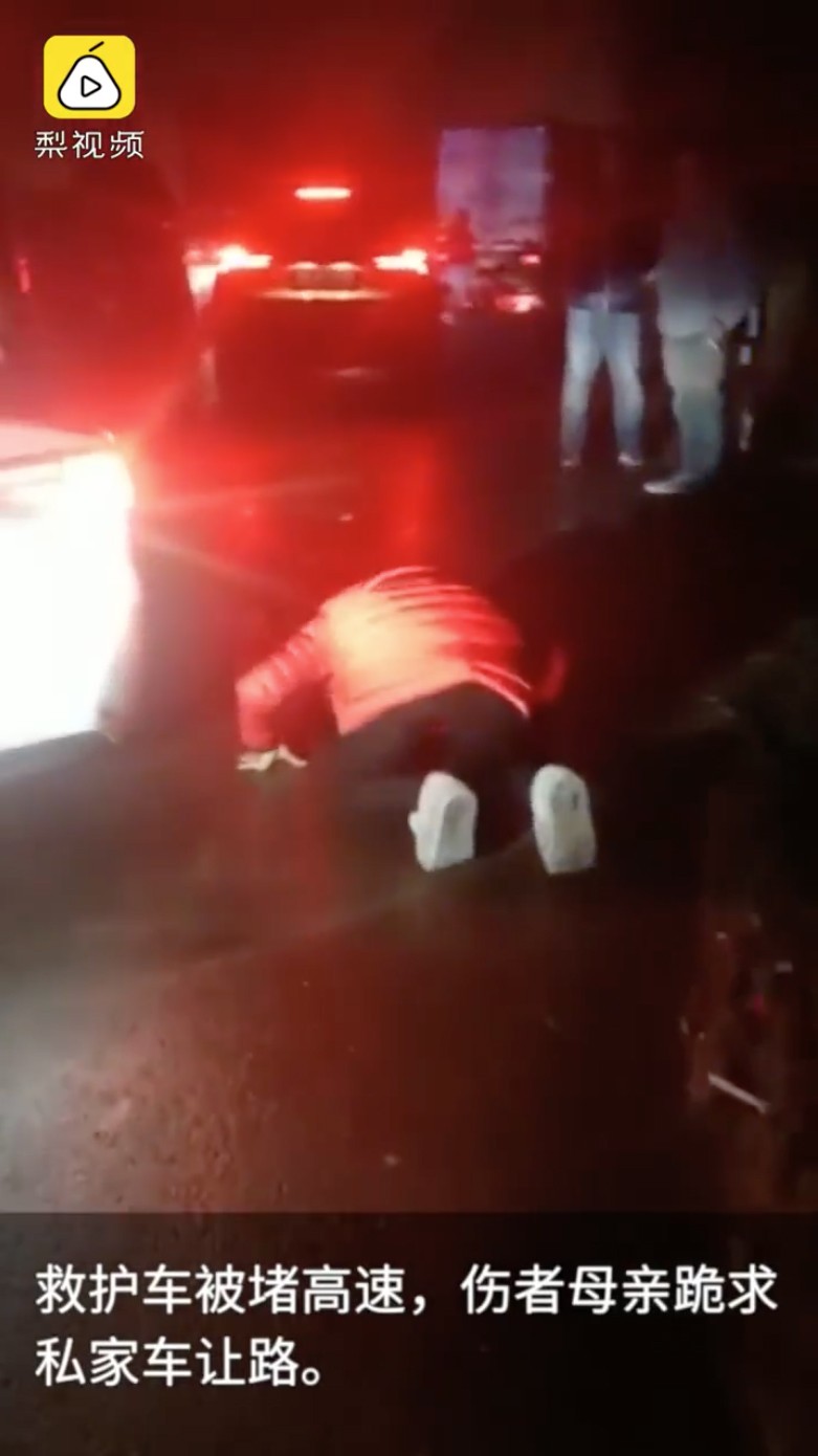 A woman gets on her hands and knees to plead with motorists to vacate an emergency lane so the ambulance carrying her injured son can get to hospital in Luan, Anhui province. Photo: Pear Video
