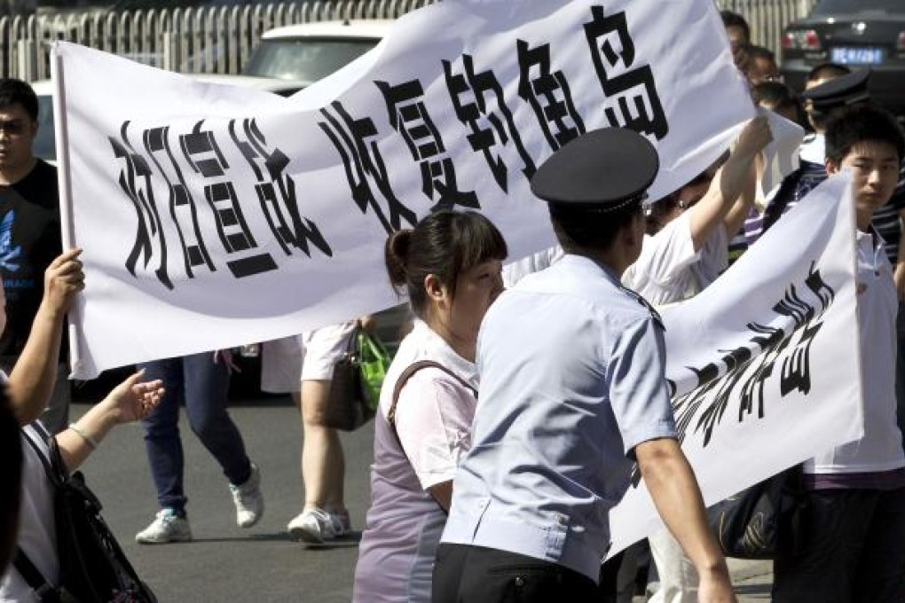 A policeman tries to control protesters as they hold a banners reading "Declare war against Japan" and "Japan get out of Diaoyu islands" outside the Japanese Embassy in Beijing Wednesday, Aug. 15, 2012. AP Photo/Andy Wong