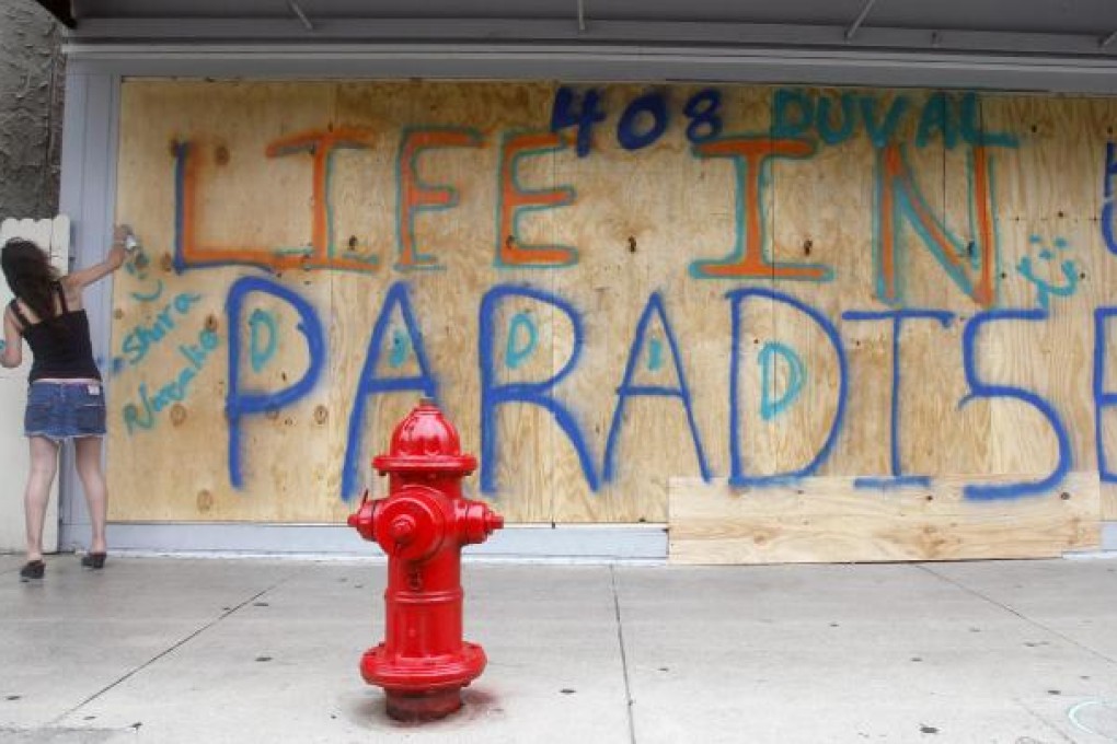 A woman puts her name on plywood protecting a storefront in anticipation of Tropical Storm Isaac. Photo: AP