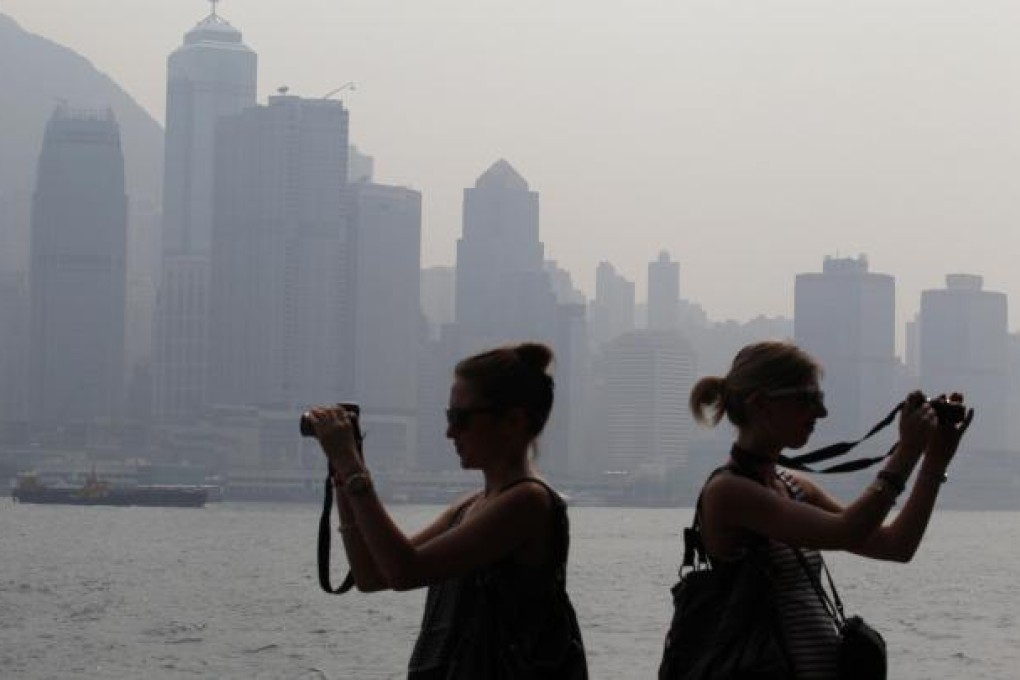 Two tourists focus their cameras to the backdrop of thick smog that has become all too familiar on Victoria Harbour. Photo: Felix Wong