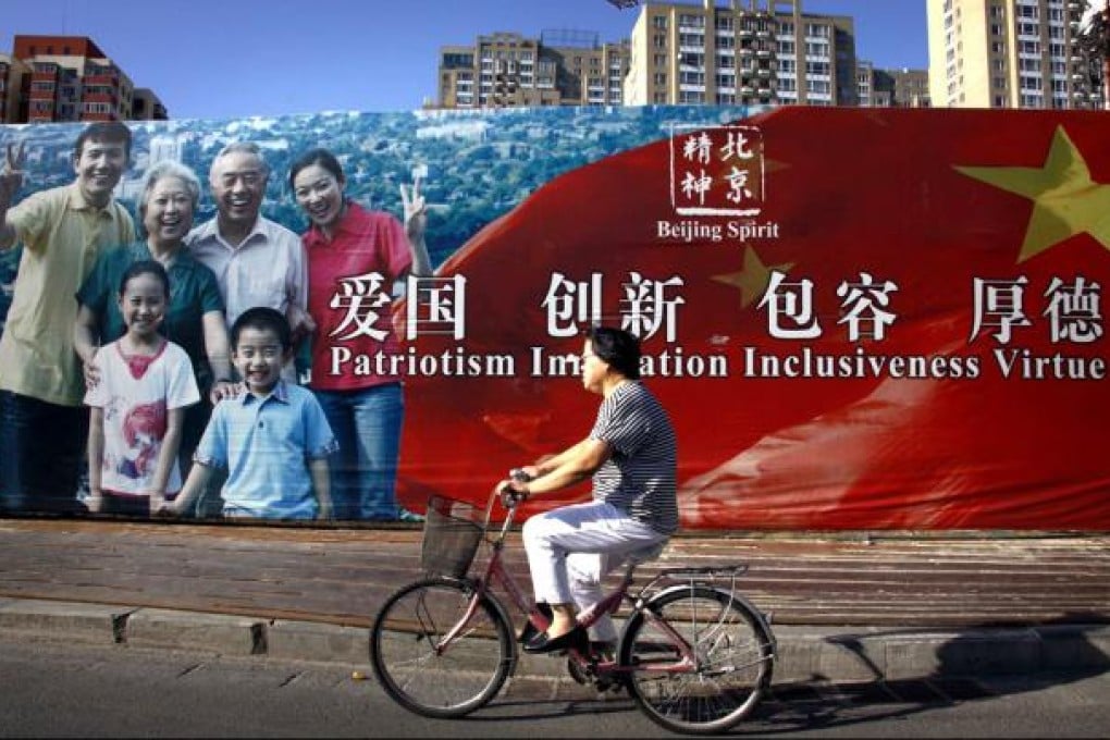 A woman rides her bicycle past a propaganda poster decorating a fence, surrounding a construction site in central Beijing. Photo: Reuters