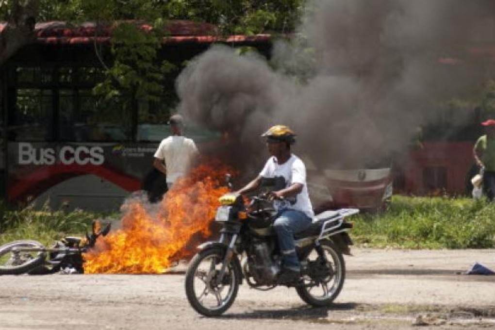 A man passes a burning motorcycle during a clash between pro-Chavez and supporters of Venezuelan opposition presidential candidate Henrique Capriles Radonski in Puerto Cabello in Venezuela
