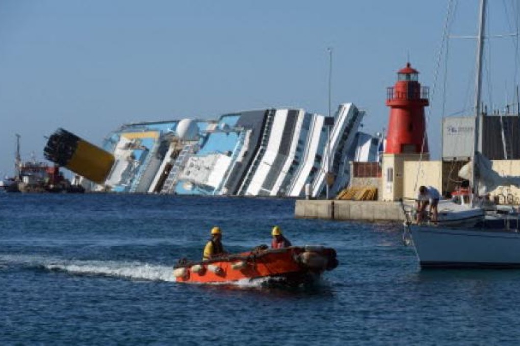 Italian salvage members entering the harbour with a view of the stranded Costa Concordia cruise ship in the background, near the Giglio Porto. Photo: AFP