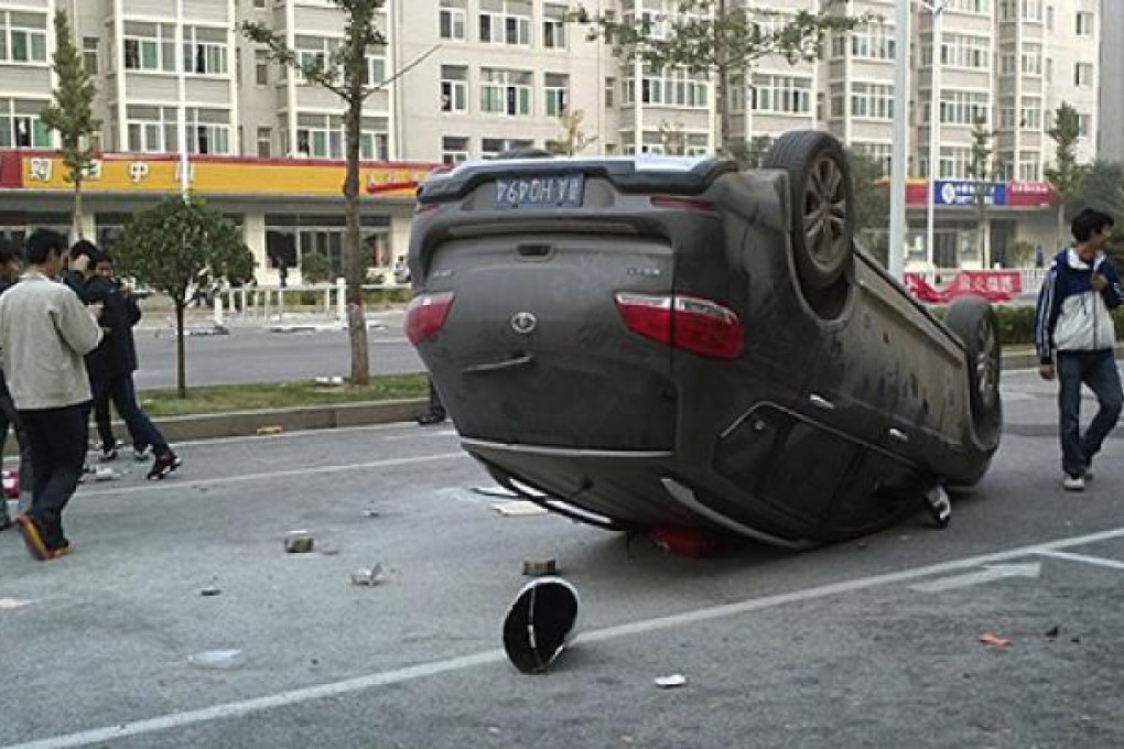 Workers take photos of a car that was turned over during a brawl by employees at Foxconn's industrial zone in Taiyuan. Photo: AP