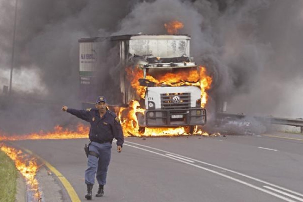 A police man reacts as flames and smoke emerge from a truck after it was set alight by striking truck drivers, near Cape Town, on Wednesday. Photo: AP