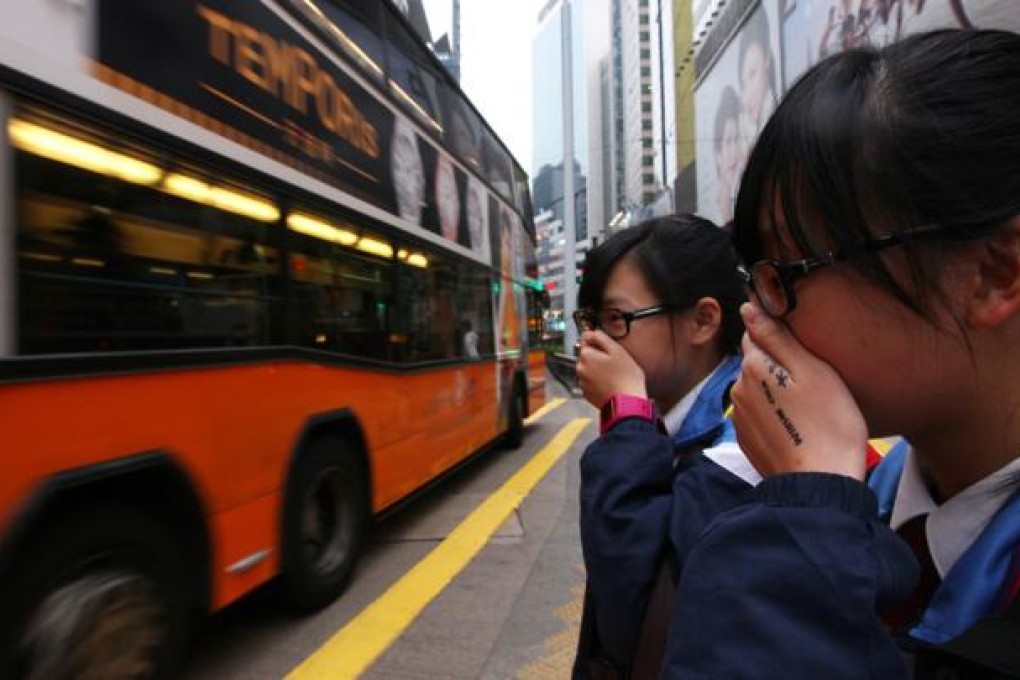 Students cover their nose to avoid emissions from vehicles as they cross Yee Wo Street in Causeway Bay. Photo: Nora Tam