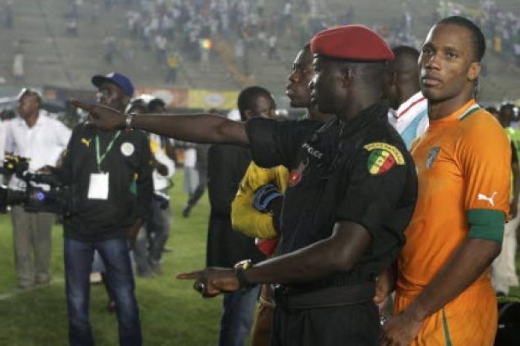A Senegalese policeman stands in front of Ivory Coast captain Didier Drogba, after rioting Senegal fans caused Ivory Coast's African Cup of Nations qualifier against Senegal to be suspended. Photo: AP