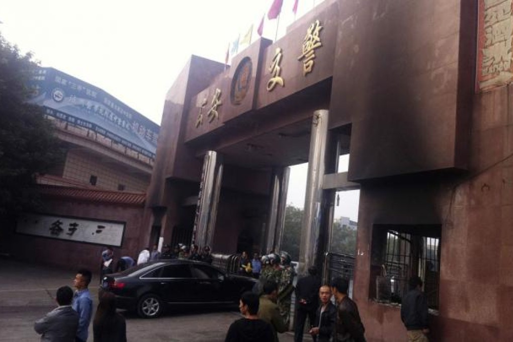 Paramilitary policemen keep guard as a car drives through a traffic police station entrance burned by protesters in Luzhou.