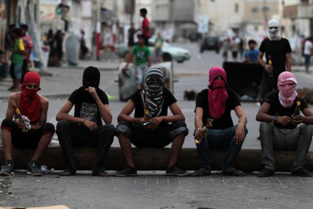 Masked Bahraini anti-government protesters holding petrol bombs sit on a telephone pole being used as a roadblock ahead of a march in Malkiya, Bahrain on Sunday, October 28. Photo: AP