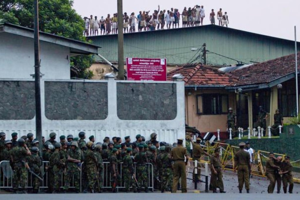 Inmates shout from the prison roof as guards assist an injured colleague (foreground right). Photo: AP