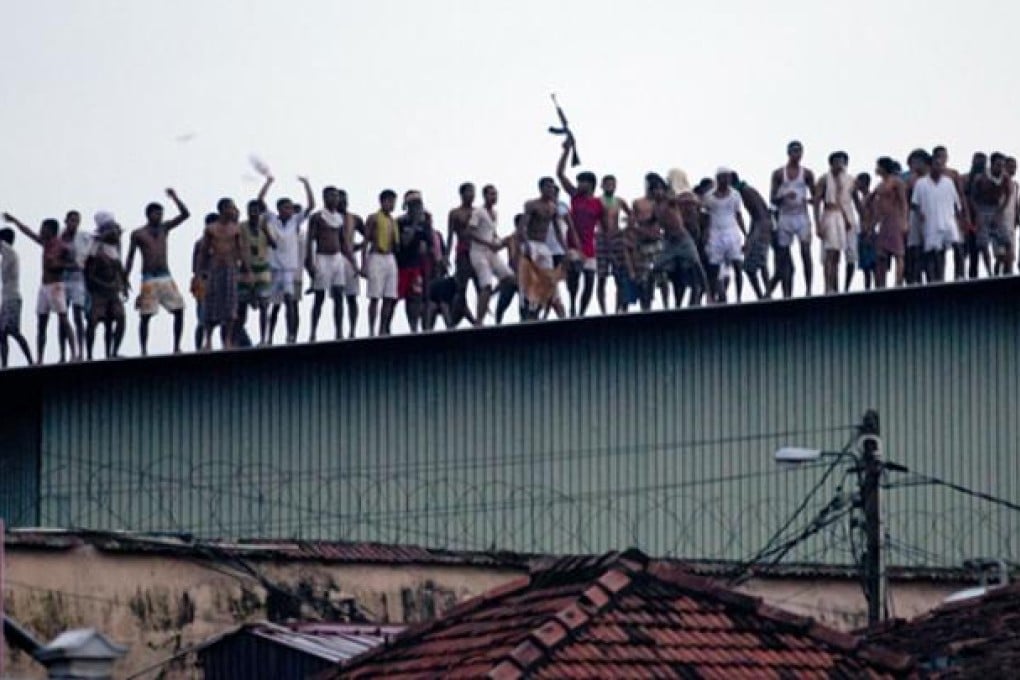 Sri Lankan inmates display guns, throw stones and shout slogans from the roof of Welikada prison in Colombo on Friday. Photo: AP