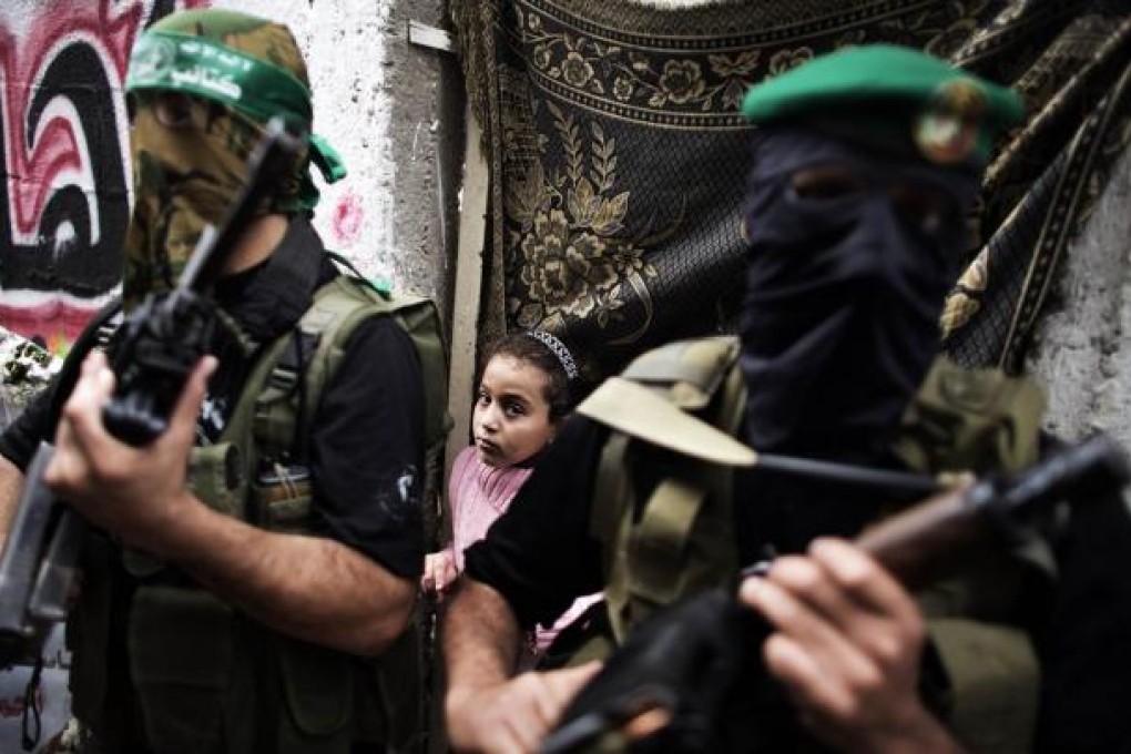 A Palestinian girl stands behind gunmen from the Ezzedine al-Qassam Brigades, the armed wing of Hamas. Photo: AFP