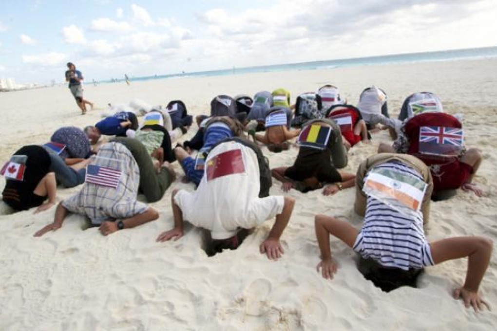 Sierra Club activists wearing flags, representing over 20 countries, take part in a climate change protest by hiding their heads in the sand in Cancun, Mexico, in 2010. Photo: AP