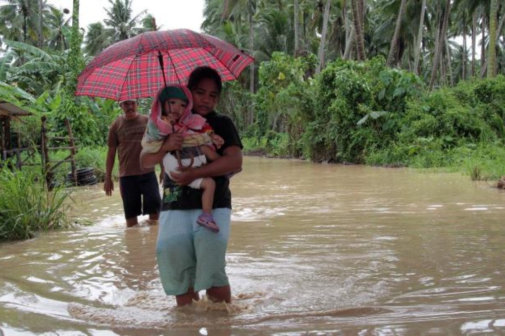 A woman carrying her child wades through a flooded road brought about by heavy rains due to Typhoon Bopha. Photo: AFP