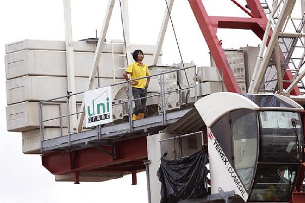 One of two construction workers protesting working conditions stands on top a crane at a building site in western Singapore. Photo: EPA
