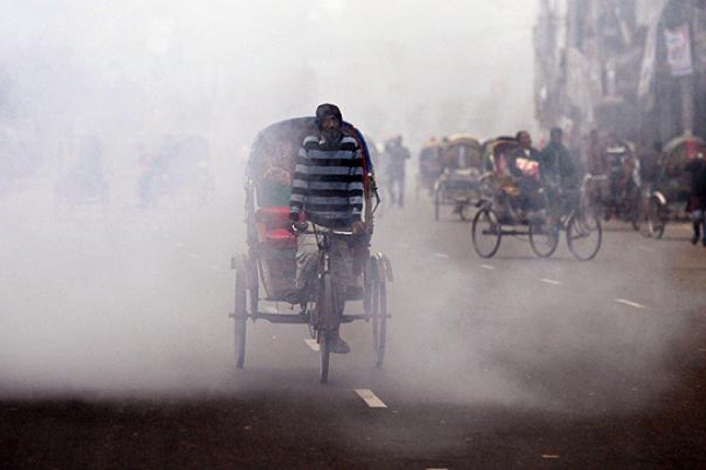 A Bangladeshi rickshaw driver cycles past the cloud of a smoke bomb during a nationwide strike in Dhaka on Tuesday. Photo: AFP