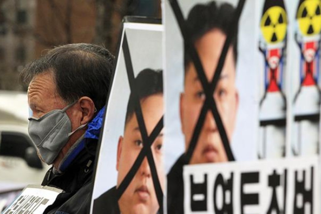 A South Korean protester sits near defaced portraits of North Korean leader Kim Jong-un during a rally denouncing North Korea's rocket launch in Seoul on Thursday. Photo: AP