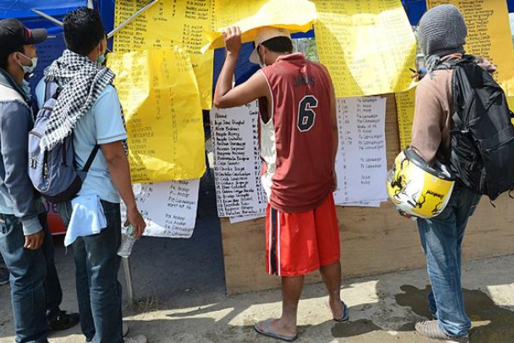 Residents look through lists of missing people posted in New Bataan. Photo: AFP
