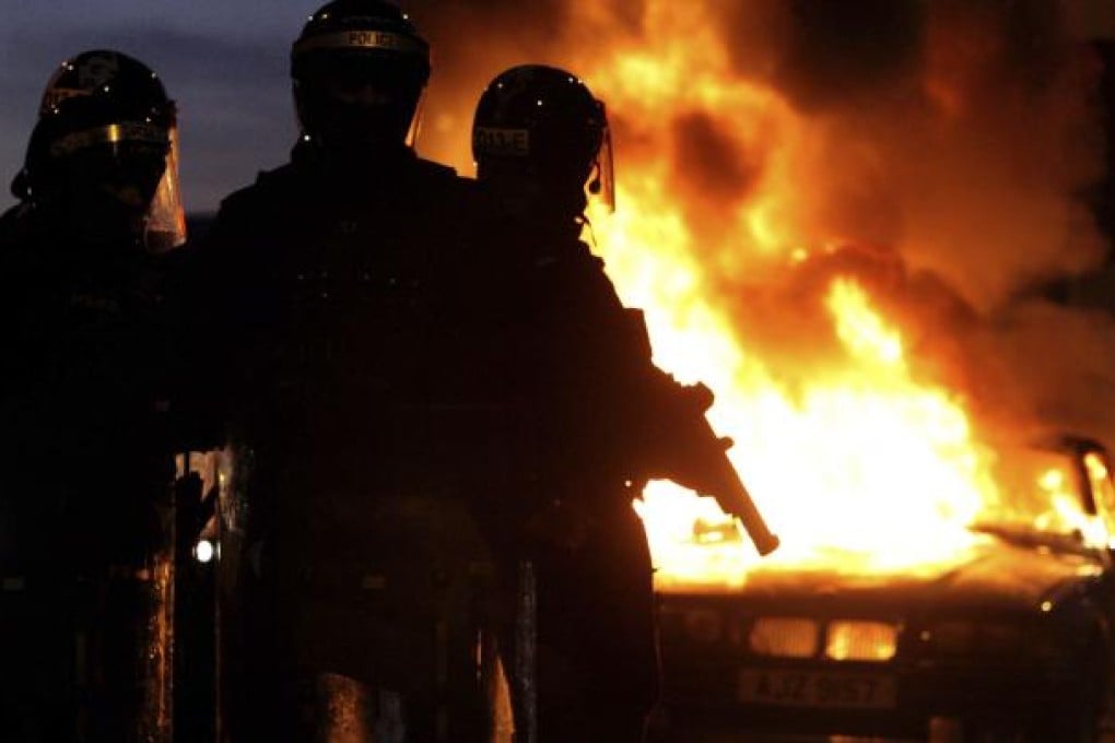 Riot police stand next to a burned out car on Saturday night, after Loyalist protesters attacked police lines, in east Belfast, Northern Ireland. Photo: AP