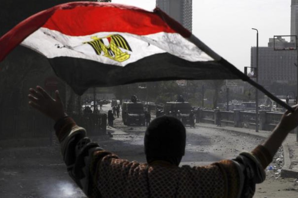 A protester opposing Egyptian President Mursi gestures at the riot police while holding the national flag during clashes along Qasr Al Nil bridge leading to Tahrir Square in Cairo. Photo: Reuters