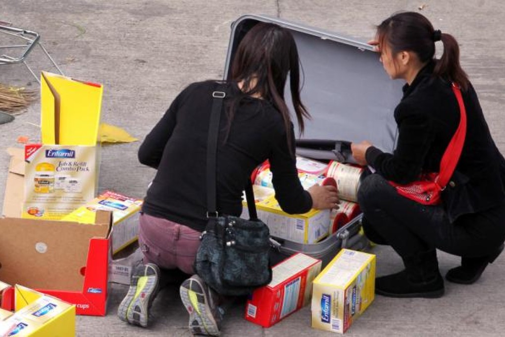 Travellers repackage cartons of baby formula outside Sheung Shui train station in an apparent attempt to evade the government's limits on the amount of the product they are allowed to take across the border. Photo: Nora Tam