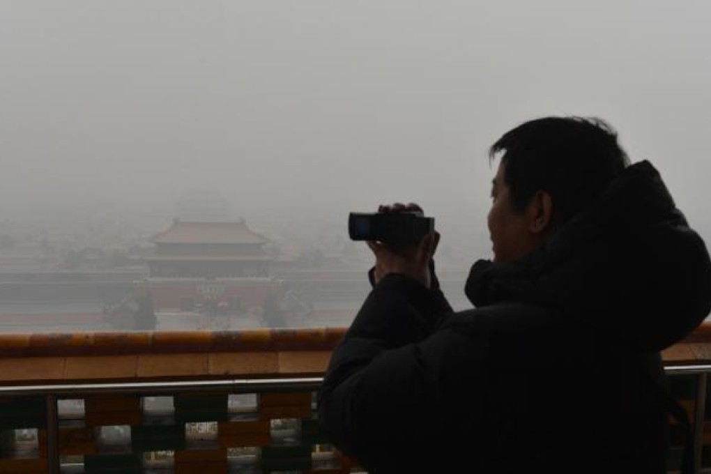 A Chinese tourist takes photos of the Forbidden City from the historic Jingshan Park as smog continues to shroud Beijing. Photo: AFP