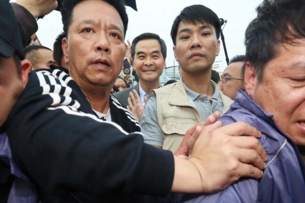 Leung Chun-ying keeps smiling as his security guards guide him through the angry mob. Photo: Sam Tsang