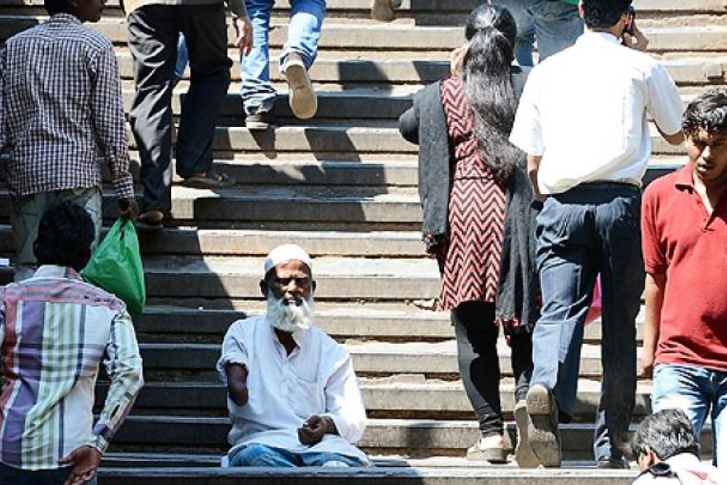 Indian pedestrians walk past a beggar sitting on the steps leading to a railway station in Mumbai. Photo: AFP