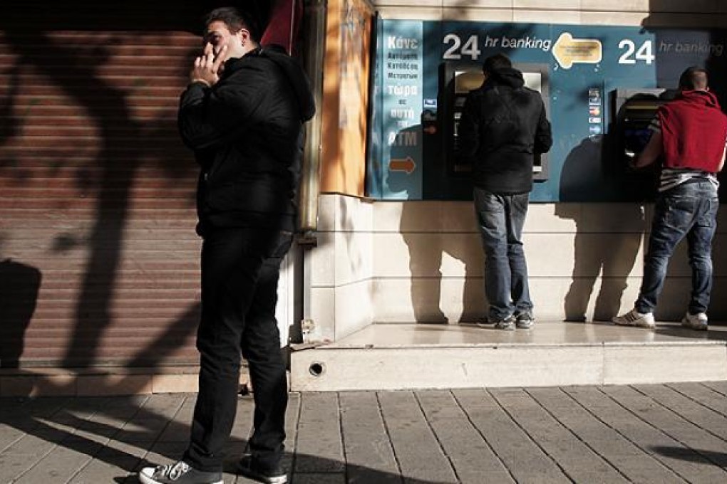 People withdraw money from an ATM machine outside a closed branch of the Bank of Cyprus in Nicosia. Photo: AP