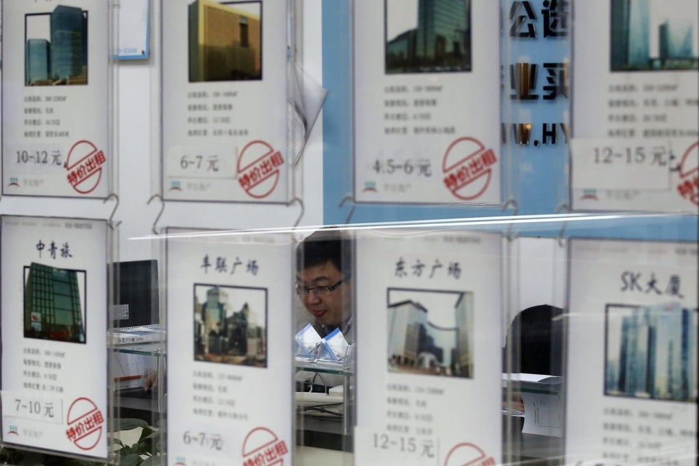 A salesman is seen through advertisements of apartments for sale at a real estate agency in Beijing. Photo: Reuters