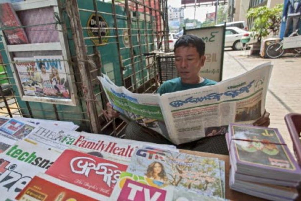 A street vendor reads a new private daily newspaper at a roadside stall in Yangon, Myanmar. Photo: EPA