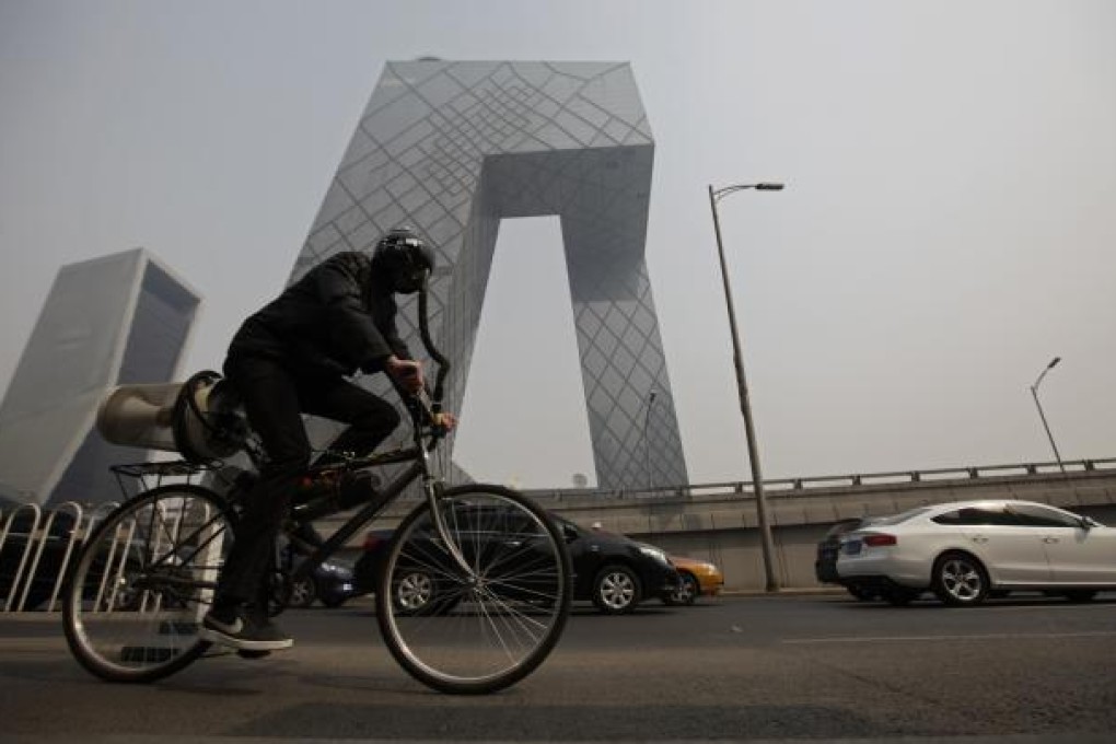 Artist Matt Hope, wearing a helmet linked to his air filtration bike, rides past the China Central Television (CCTV) building on a hazy day in Beijing. Photo: Reuters