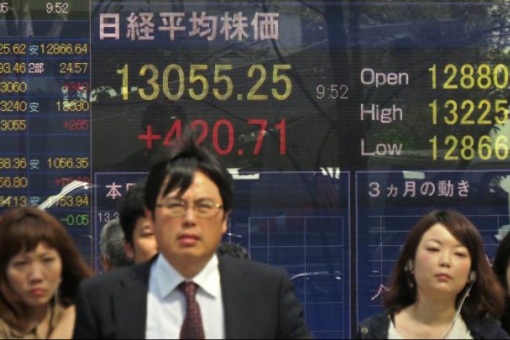 Pedestrians pass an electronic share prices board in Tokyo on Friday. Tokyo stocks jumped by more than four percent in early trade, a day after the Bank of Japan unveiled fresh easing measures that sent the yen tumbling against the dollar. Photo: AFP