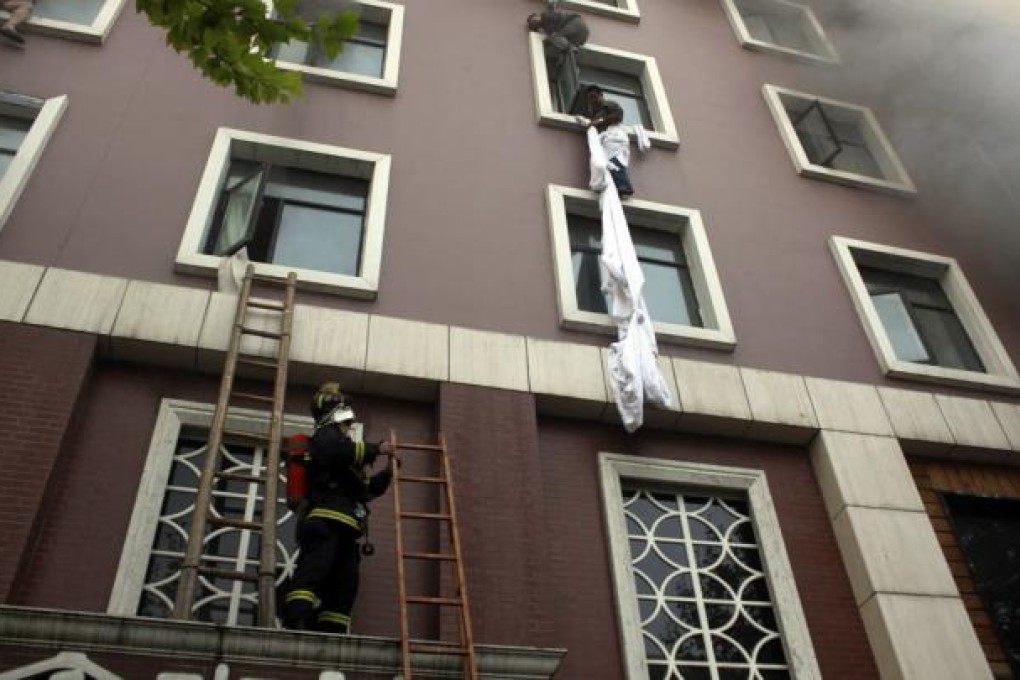 A firefighter holds a ladder as guests using sheets as ropes try to escape a hotel blaze in Xiangyang yesterday. Photo: Reuters