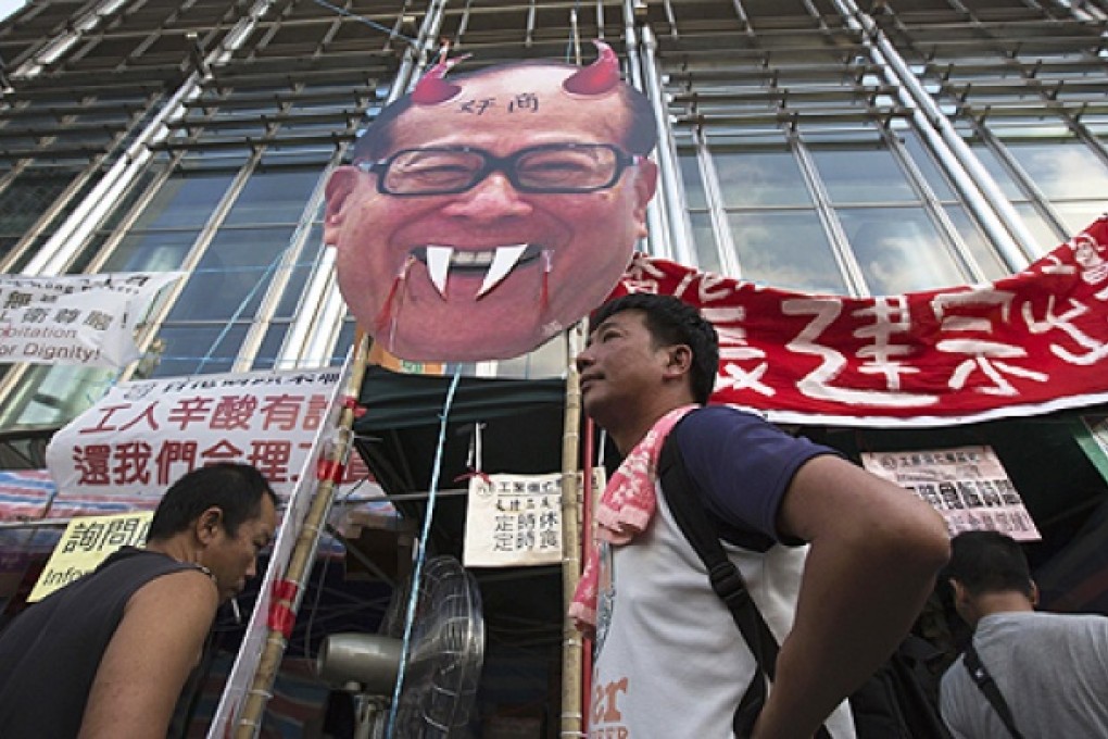 Striking dock workers stand in front of a defaced image of Li Ka-shing during a protest on Thursday. Photo: Reuters