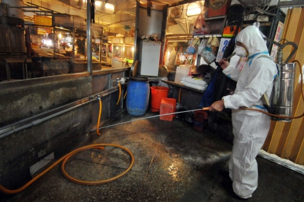 A janitor sprays disinfectant over empty poultry stalls at a traditional market. Photo: AFP