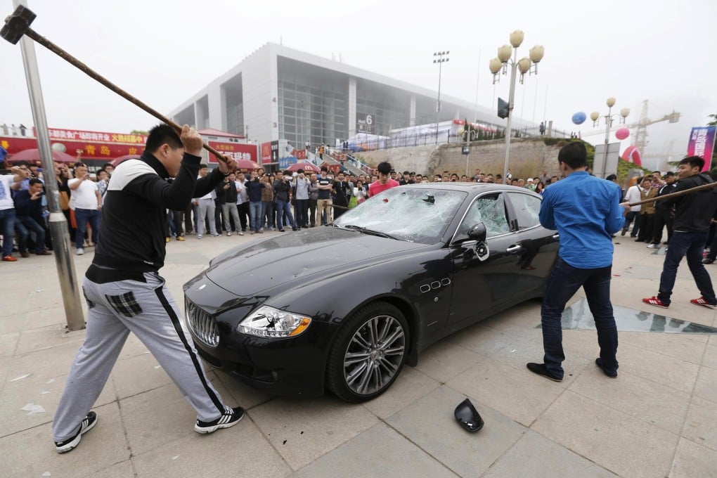 Men smash a Maserati with sledgehammers outside the Qingdao auto show in Shandong province. Photo: Reuters