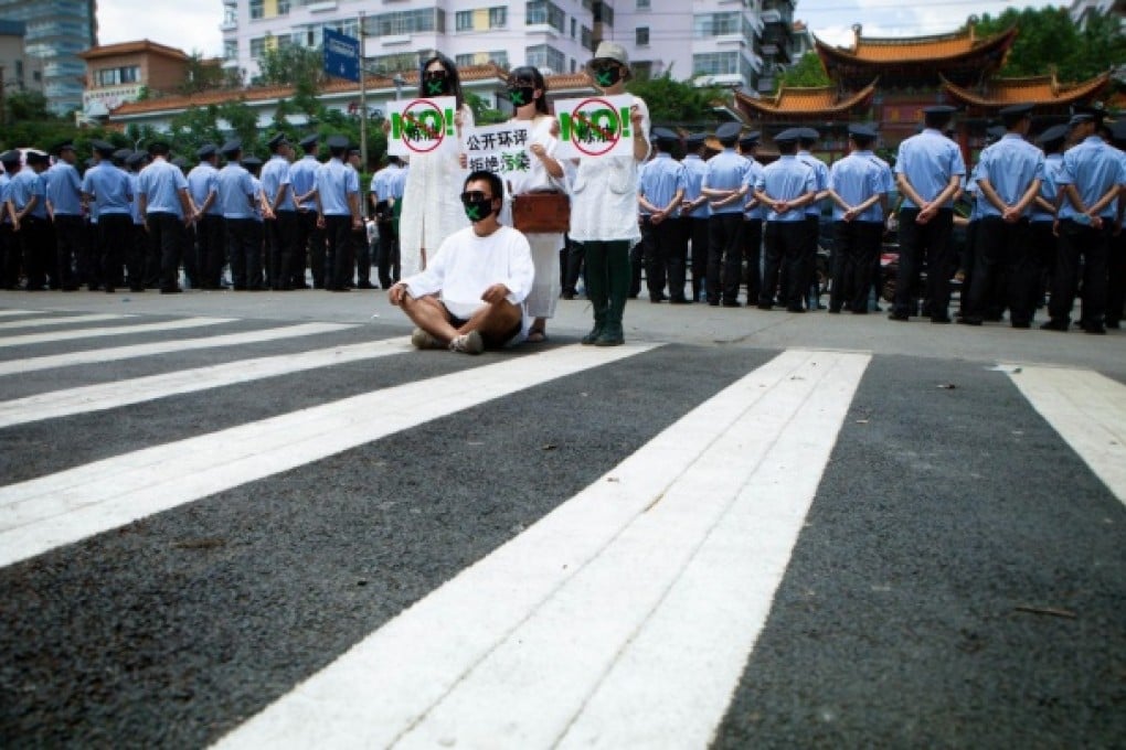 Four protesters go behind the backs of rows of police outside the government headquarters in Kunming to express their opposition to a new petrochemical plant. Photo: AFP