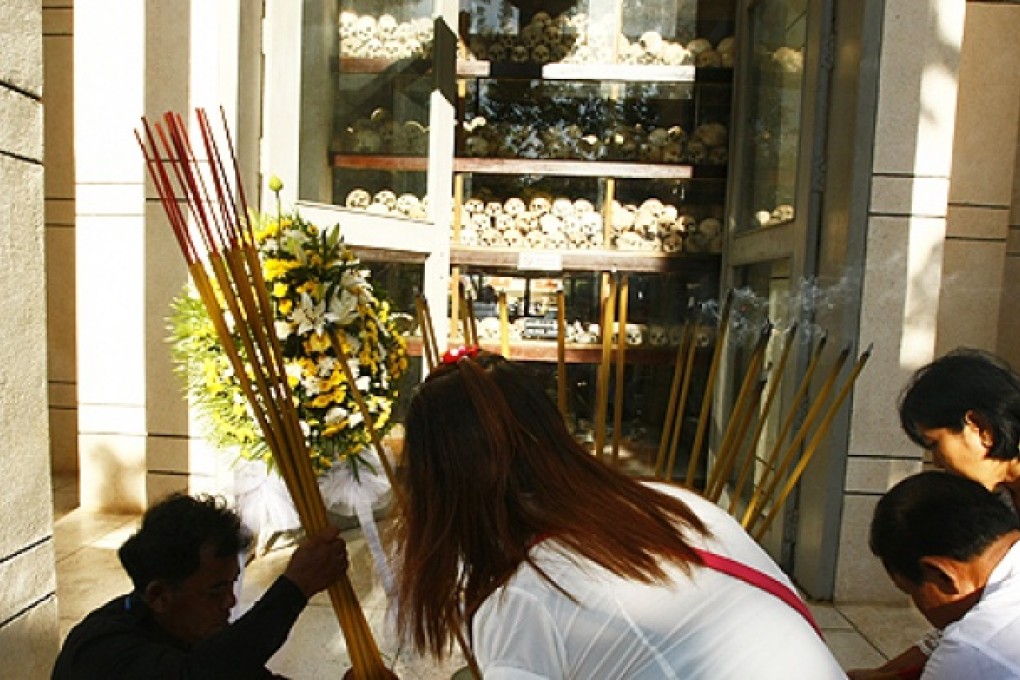 Cambodians place burning incense sticks and offer prayers at a memorial charnel housing skulls of unidentified victims of the Khmer Rouge in Choeung Ek 'Killing Field' in Phnom Penh, Cambodia. Photo: AP