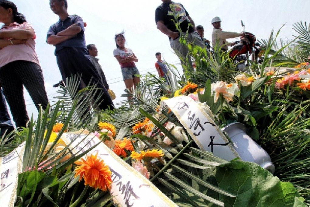 Family members of the blaze victims stand over wreaths placed on the roadside near the poultry factory yesterday. An explosion in the slaughterhouse killed at least 120 people on Monday. Photo: Simon Song