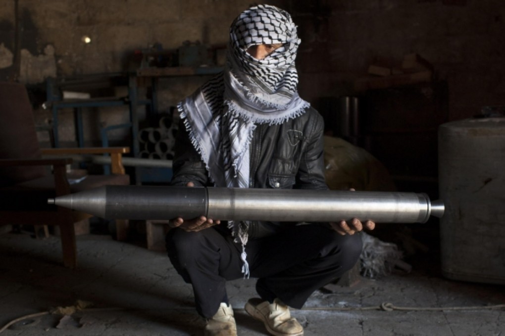 A rebel fighter holds a rocket in the metal workshop in Aleppo province where it was made. Photo: NYT