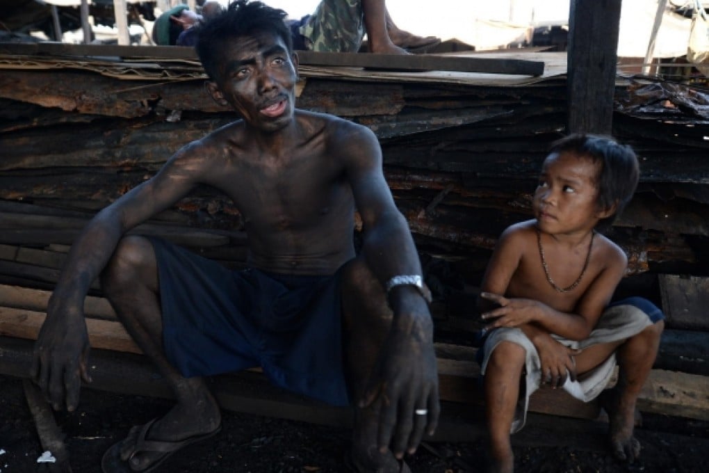 A soot-covered father and his son take a break at an unregulated charcoal factory in a Manila slum. Photo: AFP