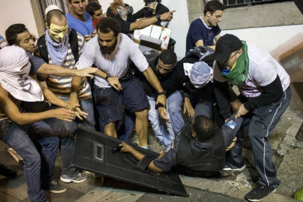 Demonstrators try to help a police officer knocked off his feet in a clash during a protest in Rio de Janeiro on Monday. Photos: AFP