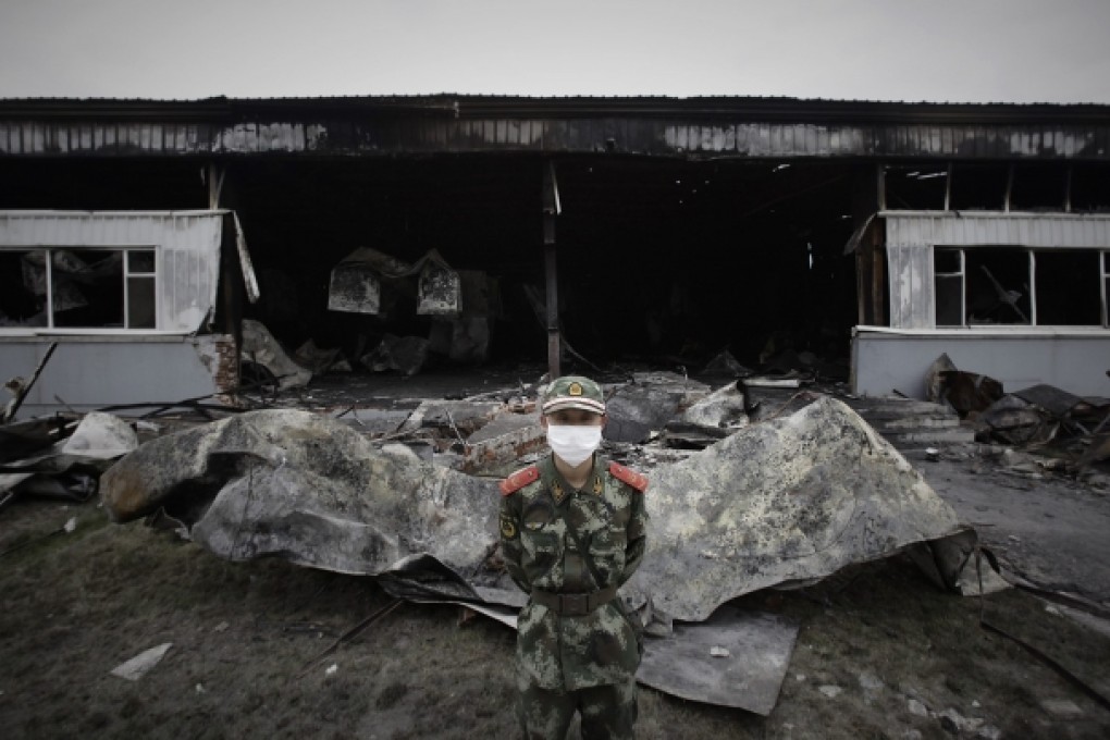 A paramilitary policeman wearing a mask stands guard in front of the burnt-out site of a poultry slaughterhouse in Dehui. Photo: Reuters